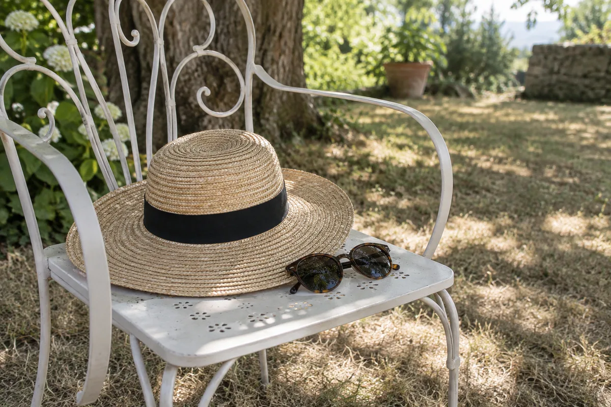 Chapeau de paille à large bord et lunettes de soleil posés sur une chaise de jardin à l’ombre